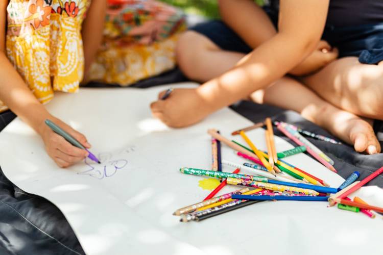 Kaksi lasta piirtämässä paperille. Etualalla väri- ja lyijykyniä. 