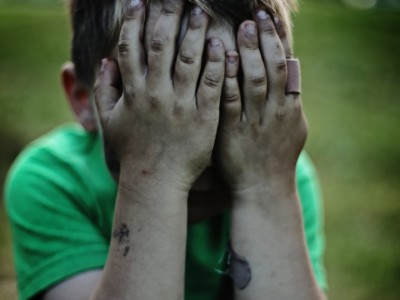 Lapsi istuu maassa peittäen kasvonsa käsillään.