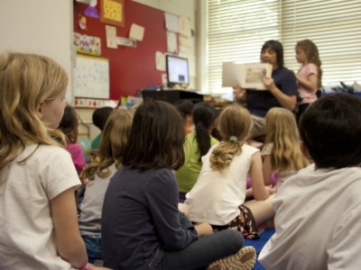 Lapset istuvat lattialla ja seuraavat opettajaa, joka näyttää heille kirjaa.