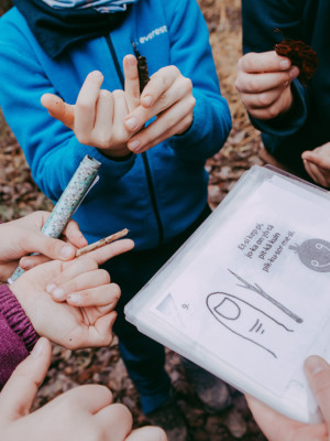 Lapset katsovat ulkona kuvakorttia, jossa neuvotaan etsimään keppi, joka on yhtä pitkä kuin pikkusormi.