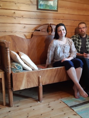 Anne Komulainen ja puolisonsa istuvat hirsitalon huoneessa puusohvalla.