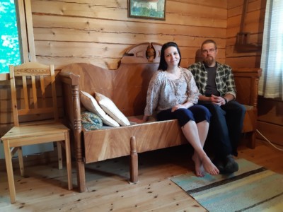 Anne Komulainen ja puolisonsa istuvat hirsitalon huoneessa puusohvalla.