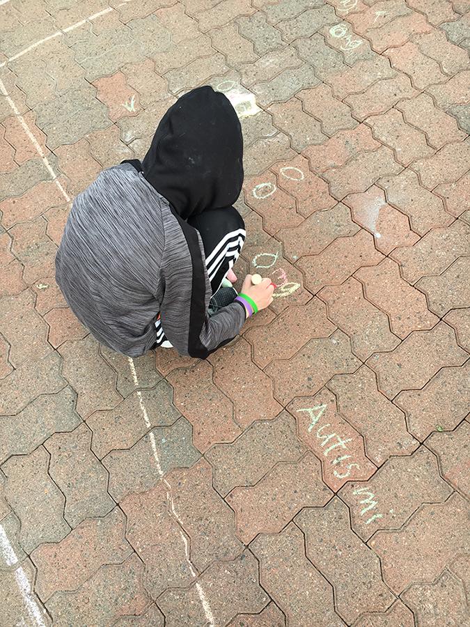 Lapsi piirtää liiduilla katuun sanaa omg. Vieressä sana Autismi.