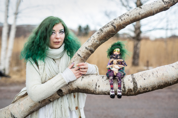 Essi Palojärvi halaa isoa puunoksaa, jolla istuu hänen näköisensä nukke.