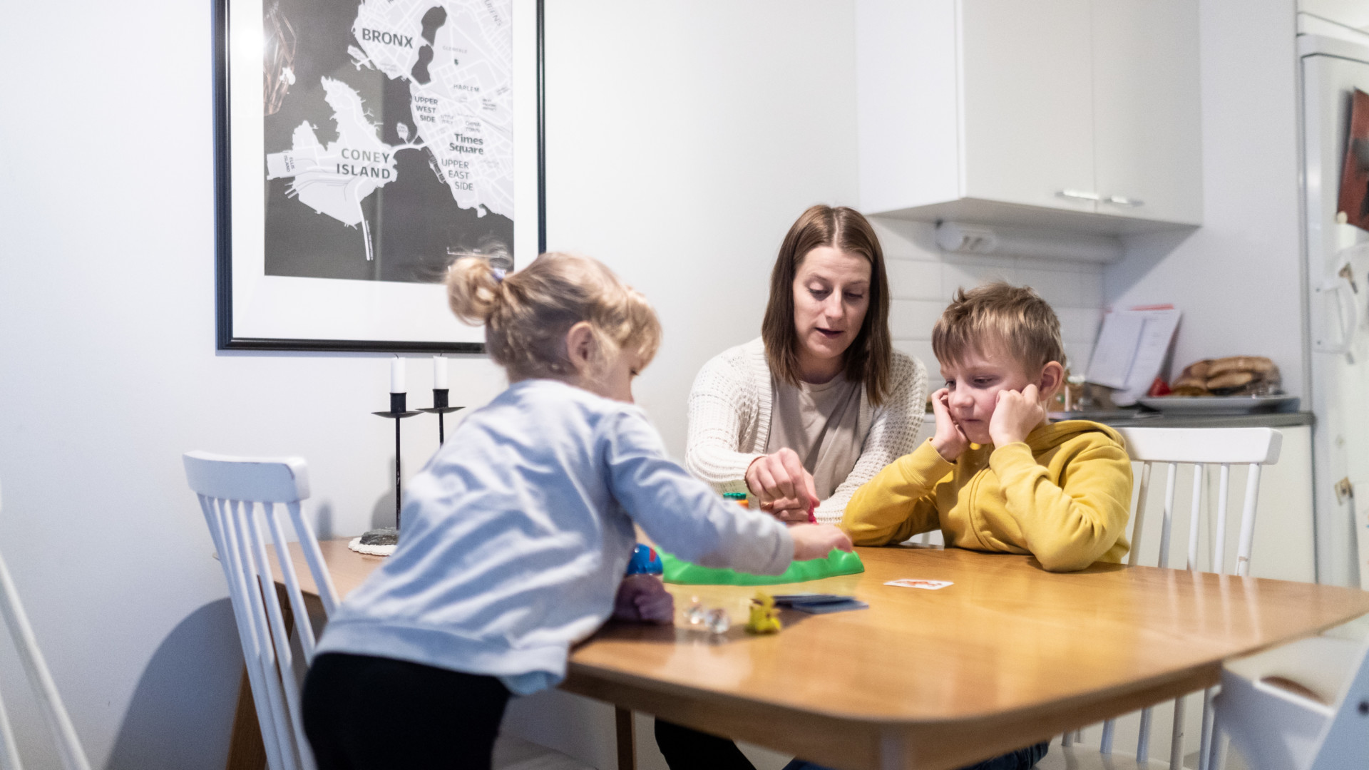 Äiti ja kaksi pientä lasta istuvat pöydän ääressä pelaamassa lautapeliä