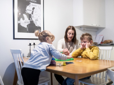 Äiti ja kaksi pientä lasta istuvat pöydän ääressä pelaamassa lautapeliä