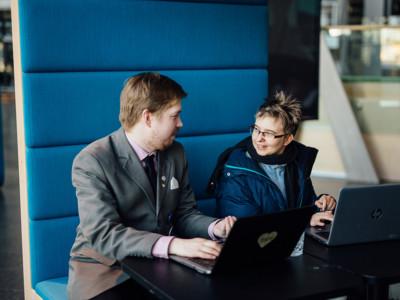 Juuso Juntunen ja Riina Noro keskustelevat. Heillä on pöydällä edessään kannettavat tietokoneet.