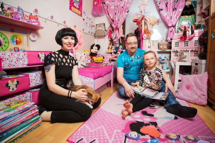 Jani, Petra ja Ida Virtanen istuvat lastenhuoneen lattialla, jossa on paljon pinkkiä ja Mikki Hiiren aiheisia asioita.