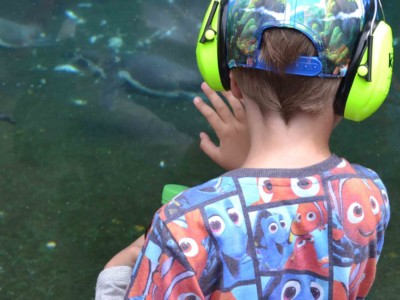 Lapsi kuulokkeet korvilla koskettaa lasia, josta heijastuu takana oleva ihminen.