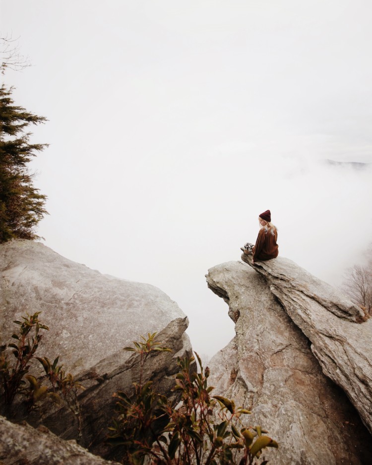 Nainen istuu kalliojyrkänteellä.