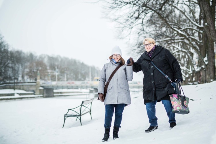 Riitta ja Marke seisovat lumihangessa ja Riitta pitää Marken kohotetusta kädestä kiinni.