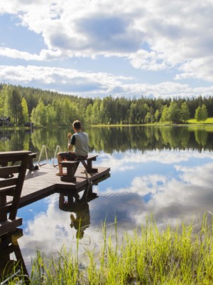 Ihminen istuu laiturilla olevalla penkillä järven rannalla.