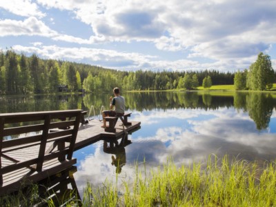 Ihminen istuu laiturilla olevalla penkillä järven rannalla.