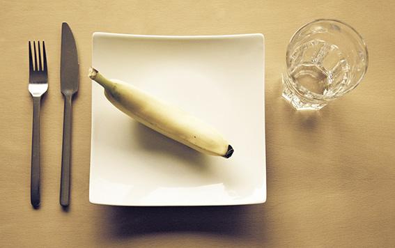 Banaani neliön muotoisella lautasella. Vieressä lasi ja aterimet.