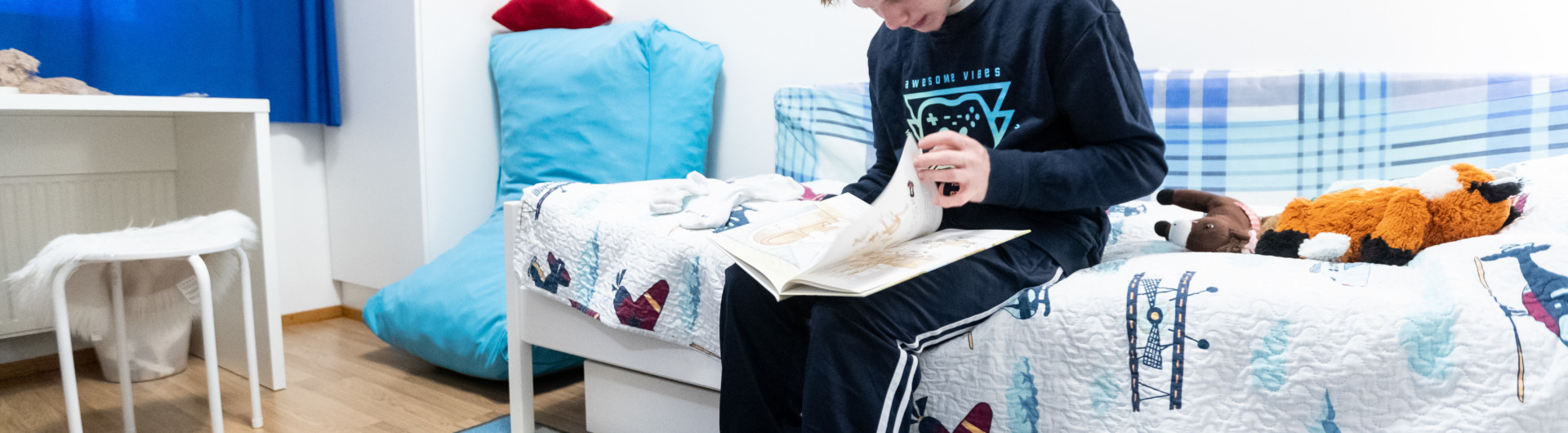Nuori mies istuu sängyllä ja katsoo kirjaa.