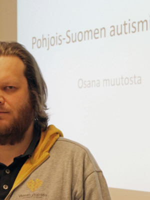 Ville Salminen vakavailmeisenä. Taustalla teksti Pohjois-Suomen Autismin kirjo ry. Osana muutosta.