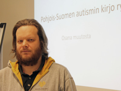Ville Salminen vakavailmeisenä. Taustalla teksti Pohjois-Suomen Autismin kirjo ry. Osana muutosta.