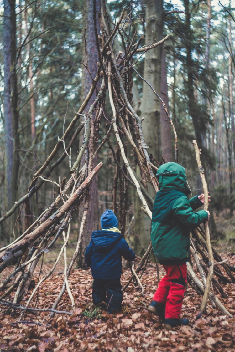 Kaksi lasta rakentaa risumajaa metsässä.