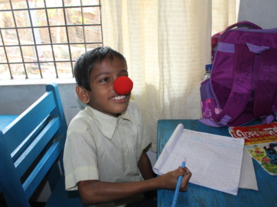 Lapsi, jolla punainen klovnin nenä, tekee koulutehtäviä pöydän ääressä.