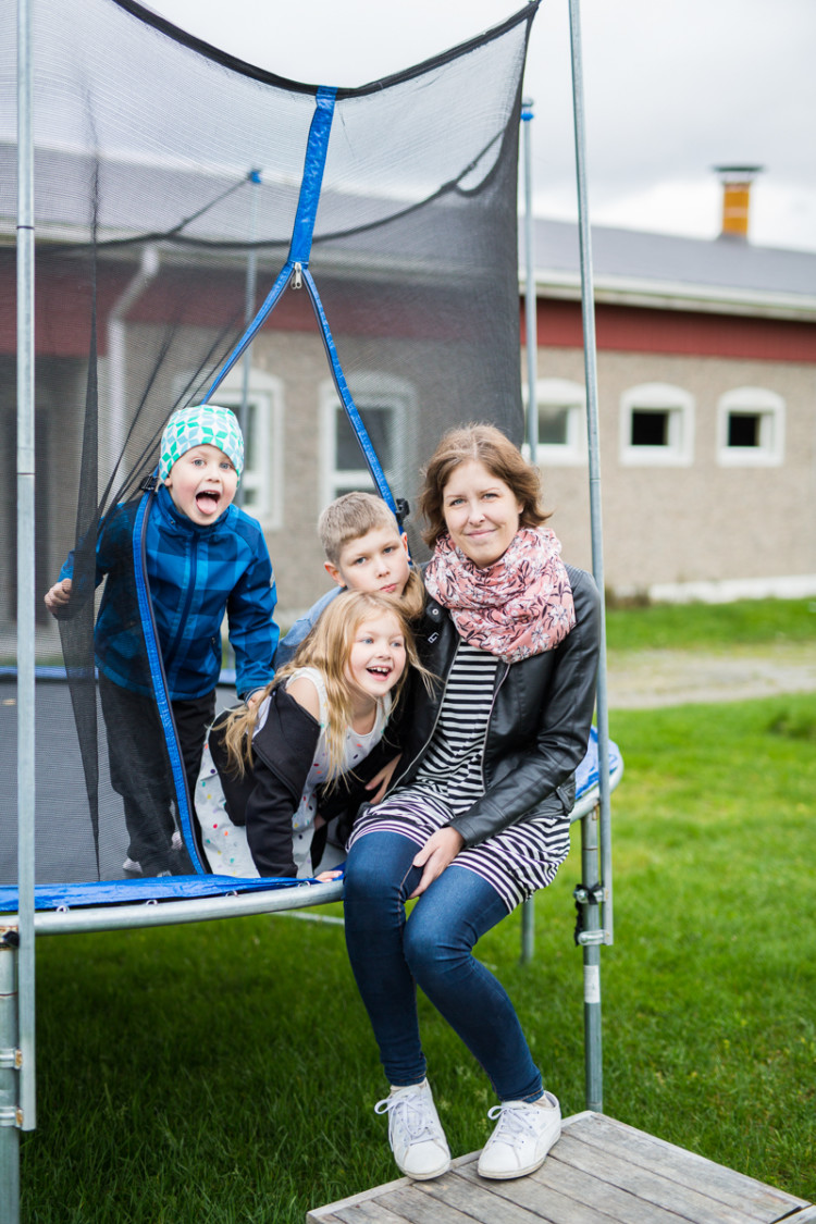 Nainen istuu kolmen lapsen kanssa trampoliinilla.