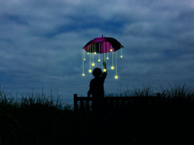 Ihmishahmo pimeässä pitää kädessä sateenvarjoa, josta roikkuvat tähdet.