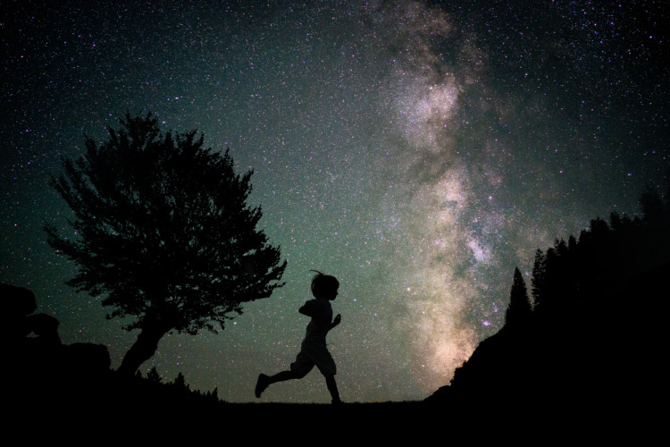 Lapsi juoksee pimeässä tähtitaivaan alla.