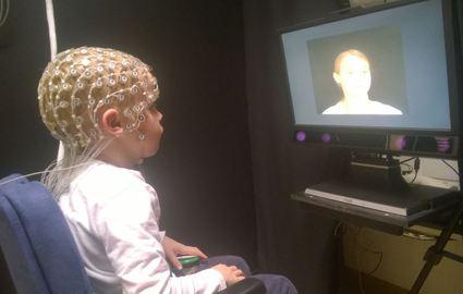 Lapsi istuu elektrodit päässään ja katsoo näytöllä olevaa kasvokuvaa.