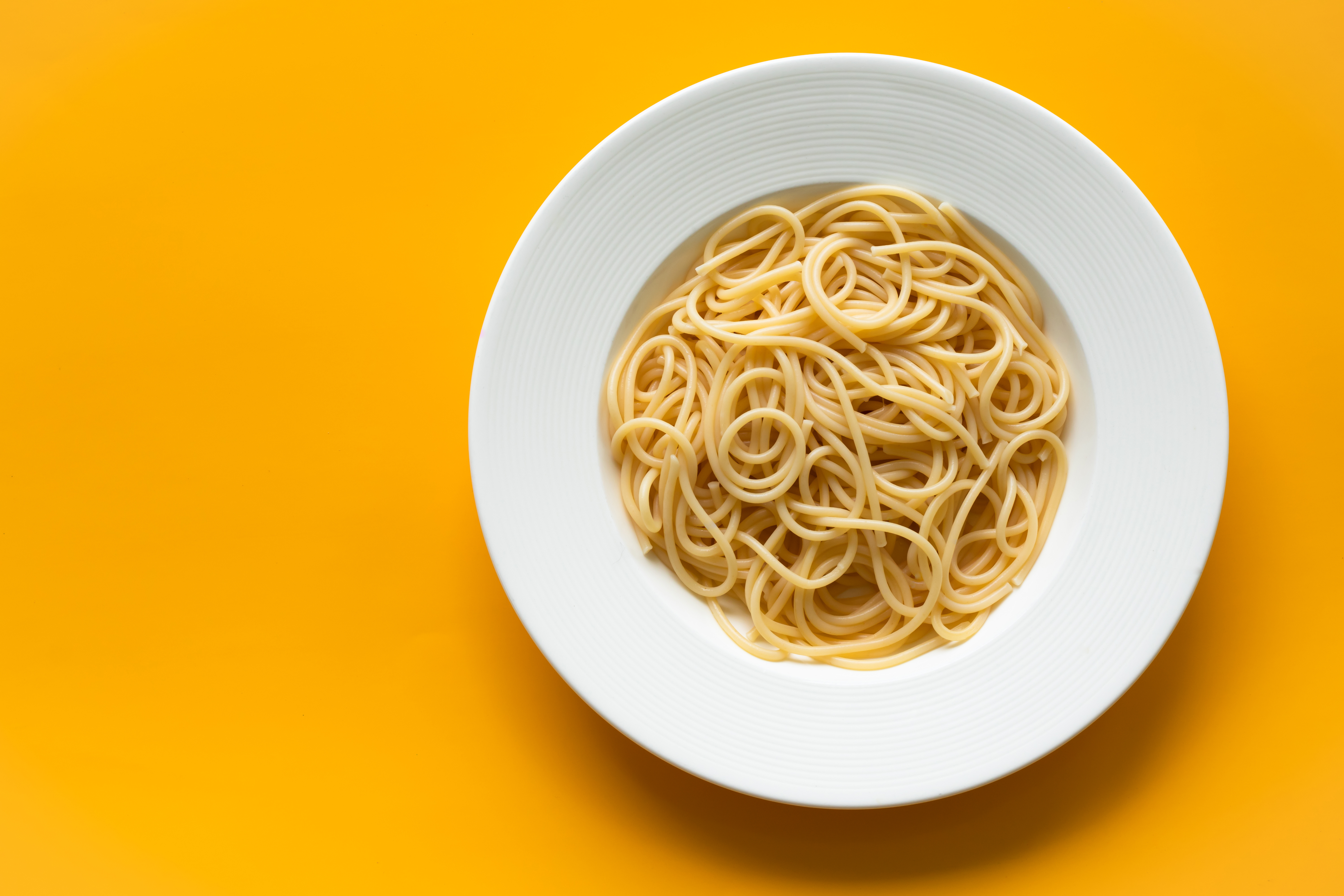 Keitettyä spagettia lautasella. Keltainen tausta.