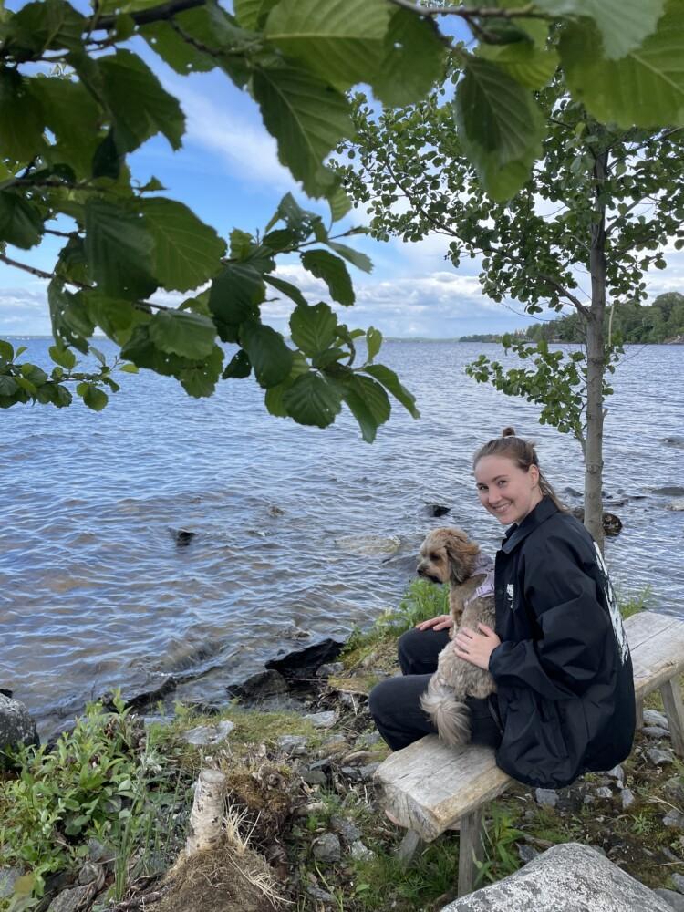 Jenna Arvola istuu penkillä tuulisena päivänä vesistön äärellä. Sylissä koira.