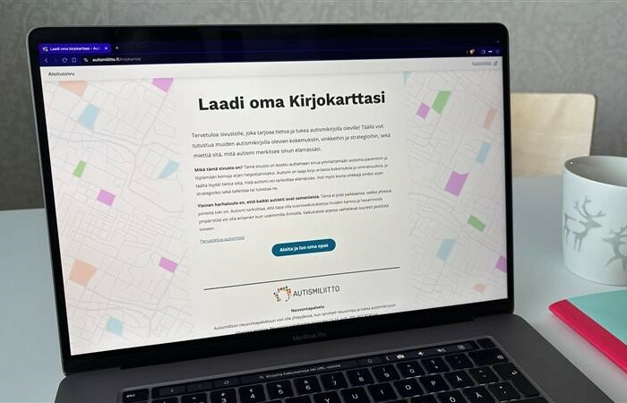 Pöydällä kannettavan tietokoneen ruudulla on auki Kirjokartta-sivuston etusivu, jossa lukee isolla Laadi oma kirjokarttasi. Pöydällä myös muki ja jonkun vihkon reuna.