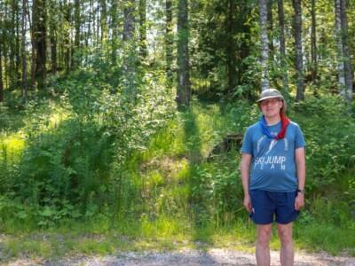 Mies lippiksellä ja partiohuivilla seisoo kesän vehreydessä metsän laidalla.