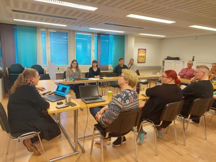Ihmisiä istumassa kokouspöydän ääressä.