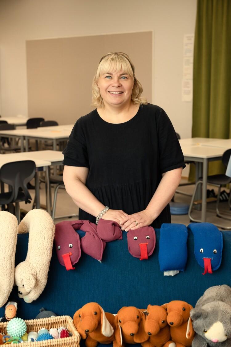 Eveliina Nikunlassi seisoo koululuokassa sohvan takana. Sohvalla erilaisia paino- ja aistivälineitä.