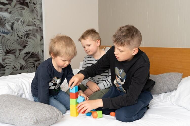 Kolme poikaa sängyllä rakentamassa palikkatornia.