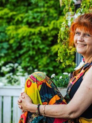 Tuula Niinikangas istuu terassin kasvillisuuden keskellä värikkäässä mekossa.