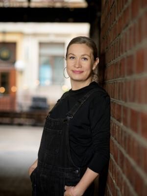 Laura Huuskonen seisoo porttikäytävässä ja nojaa tiiliseinään.