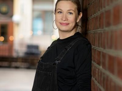 Laura Huuskonen seisoo porttikäytävässä ja nojaa tiiliseinään.