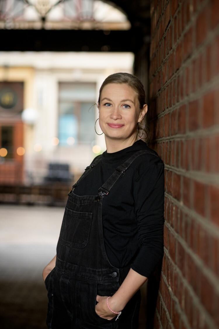 Laura Huuskonen seisoo porttikäytävässä ja nojaa tiiliseinään.