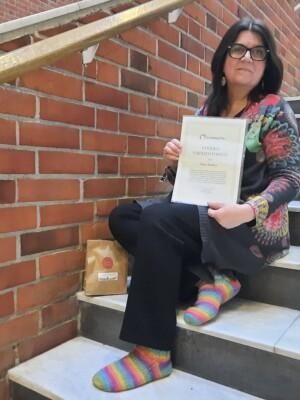 Maria Kuoksa istuu portailla ja hänellä on kädessään vuoden vapaaehtoisen kunniakirja.