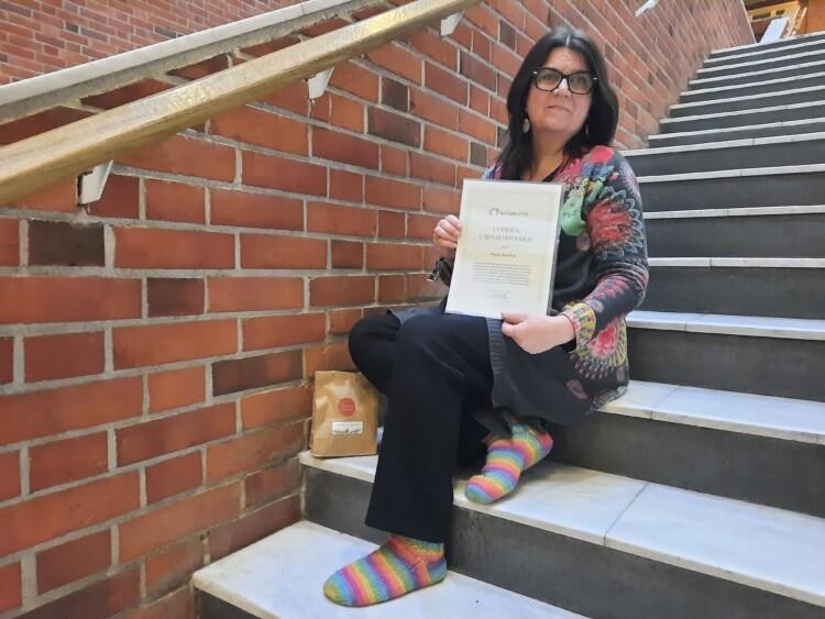 Maria Kuoksa istuu portailla ja hänellä on kädessään vuoden vapaaehtoisen kunniakirja.