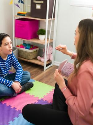 Aikuinen puheterapeutti työskentelemässä lattialla istuvan pojan kanssa.