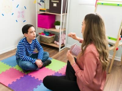 Aikuinen puheterapeutti työskentelemässä lattialla istuvan pojan kanssa.