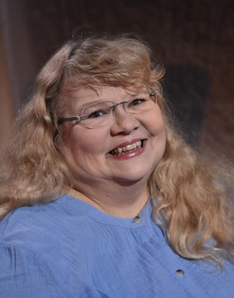 Kuvassa hymyilevä Annikka Suoninen. Hänellä on sininen paita, vaalea, pitkä, hieman kihara tukka ja lismälasit.
