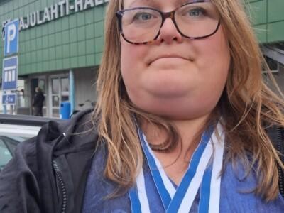 Ruskeatukkaisella naisella on silmälasit ja kaulassa roikkuu kaksi mitalia.