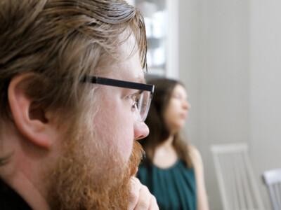Lähikuvassa parrakas mies, jolla silmälasit. Taustalla sumeampana nainen.