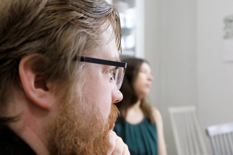 Lähikuvassa parrakas mies, jolla silmälasit. Taustalla sumeampana nainen.
